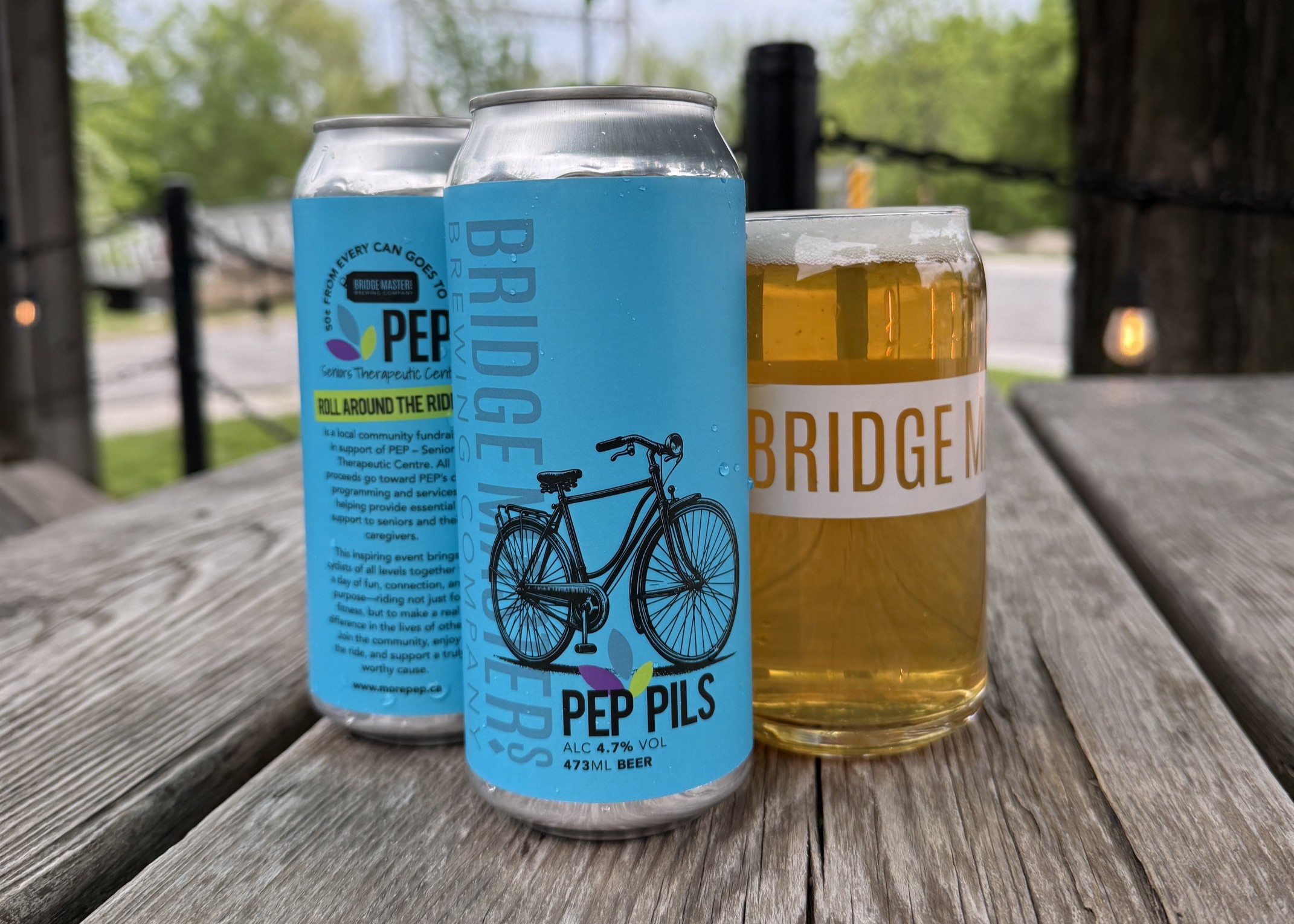 Draft can sleeve for PEP Pils by Bridge Masters Brewing: turquoise label with bicycle art, Roll Around the Rideau banner, and note that fifty cents from each can supports PEP Seniors Therapeutic Centre